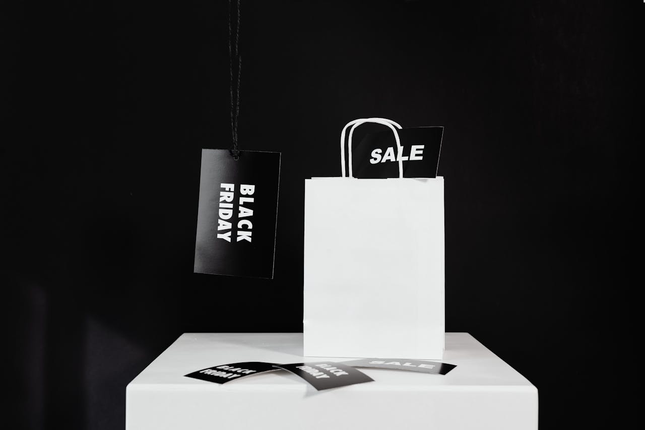 White shopping bag on a minimalist stand with Black Friday and sale tags on a dark background.
